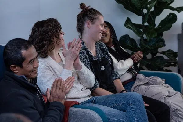 Four people similing and clapping while sitting on a sofa