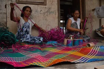 Two people weaving a colourful rug