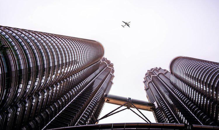 A view looking up at skyscrapers with a plane flying overhead