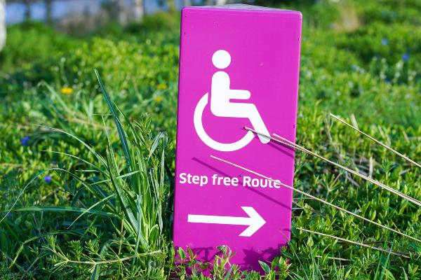 Pink sign with an outline of a person in a wheelchair and text saying 'step free route'