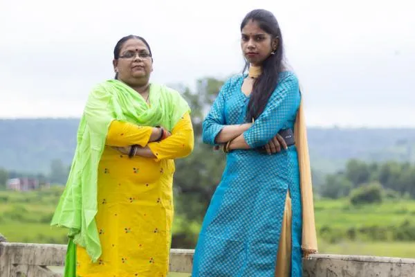 Two women wearing saris standing next to each other with arms folded