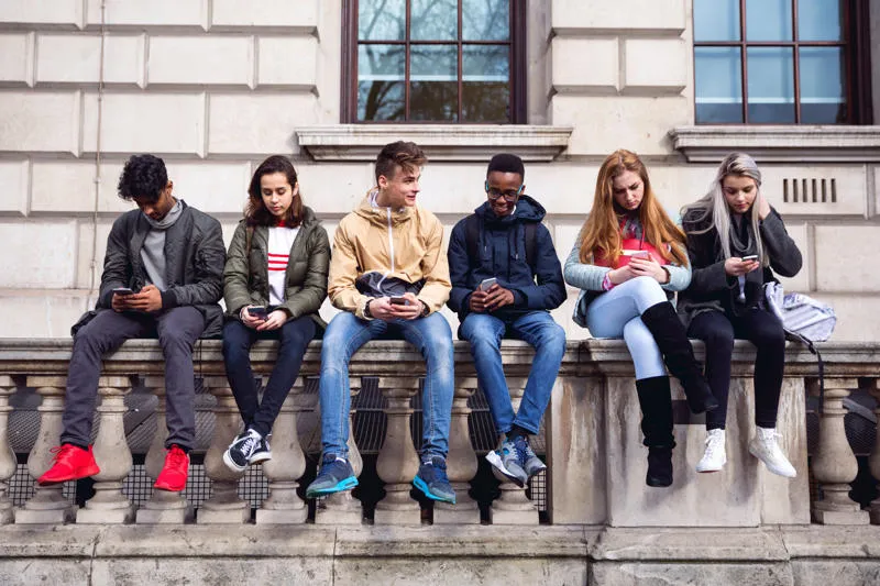 A group of young people sitting on a wall using their mobiles