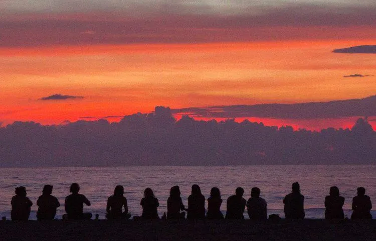 Silhouettes of people sitting on a beach watching a sunset