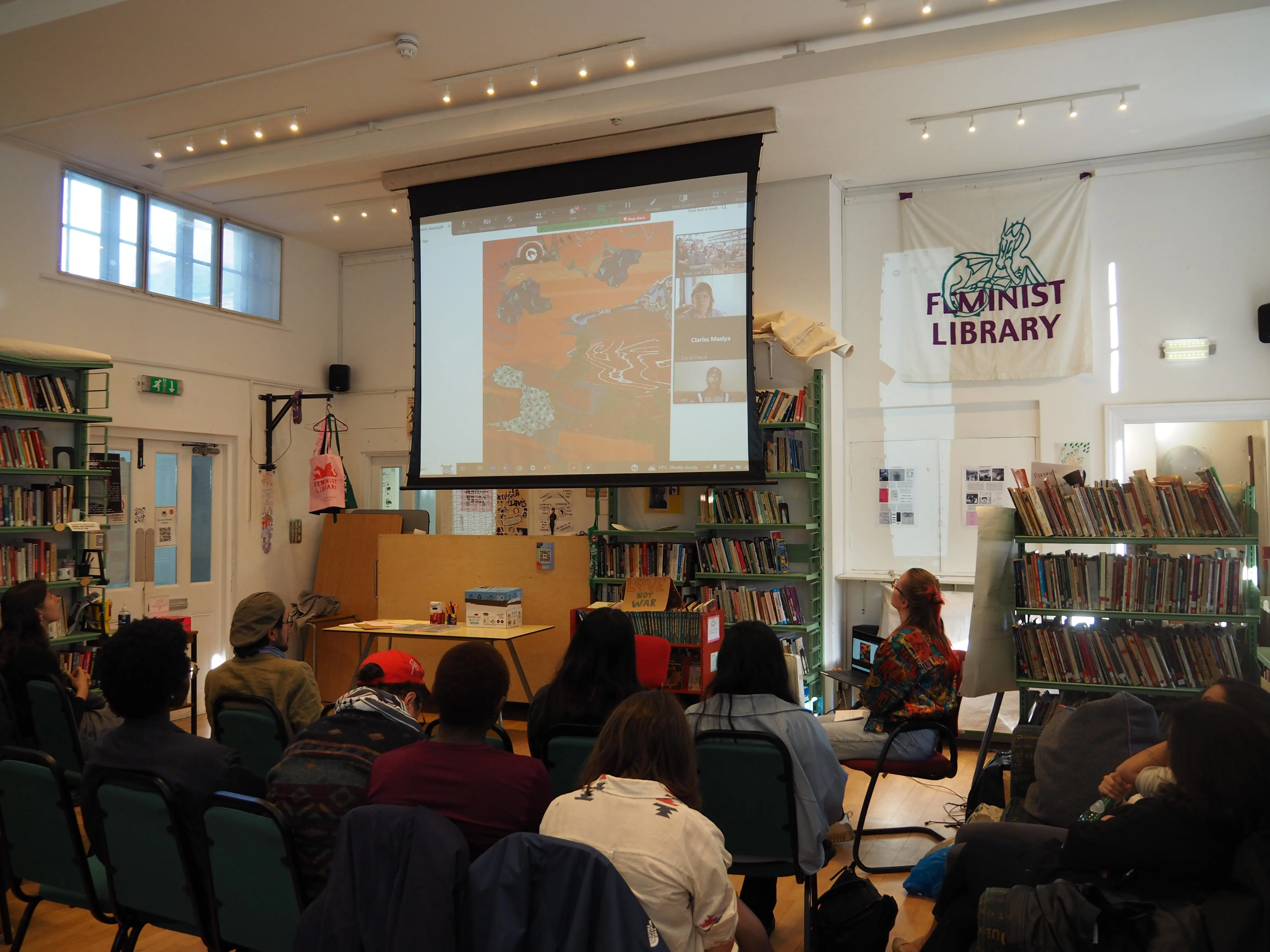 An audience watching an artwork and virtual participants on a projector screen 