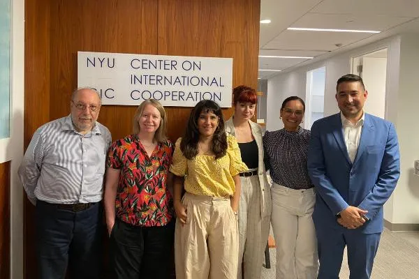 Image of a group of people standing in front of a sign that says 'NYU Center on International Cooperation'